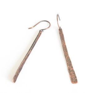May include: A pair of long, hammered copper earrings with a rustic finish. The earrings are a simple, yet elegant design, perfect for everyday wear.