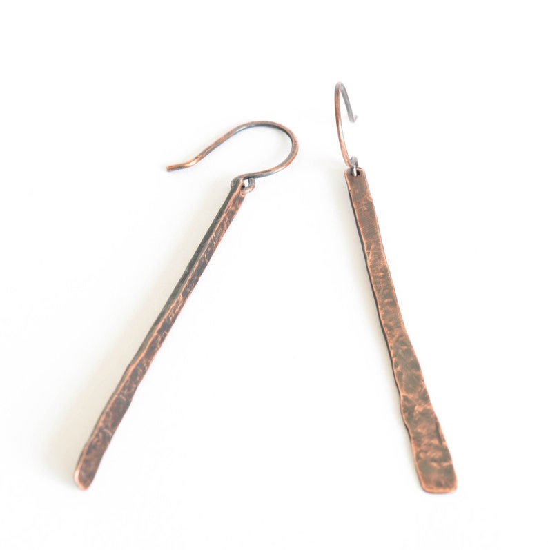 May include: A pair of long, hammered copper earrings with a rustic finish. The earrings are a simple, yet elegant design, perfect for everyday wear.