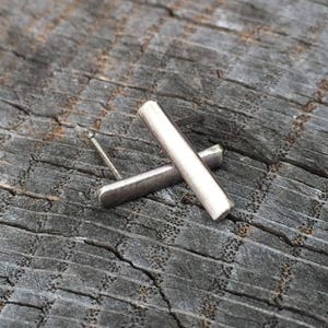 May include: A pair of silver bar earrings. The earrings are simple and modern, with a brushed finish.