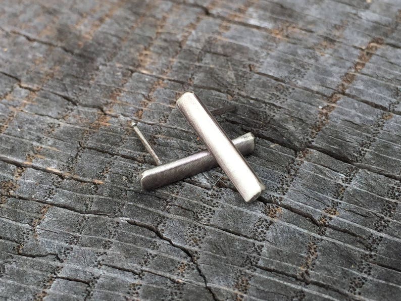 May include: A pair of silver bar earrings. The earrings are simple and modern, with a brushed finish.
