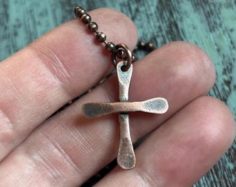 Puede incluir: Un colgante de cruz de cobre en una cadena de cobre. La cruz es simple y tiene un acabado martillado.