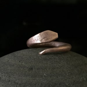 Puede incluir: Un anillo de serpiente de color cobre con un acabado texturizado. El anillo est&aacute; enrollado y la cola es puntiaguda.