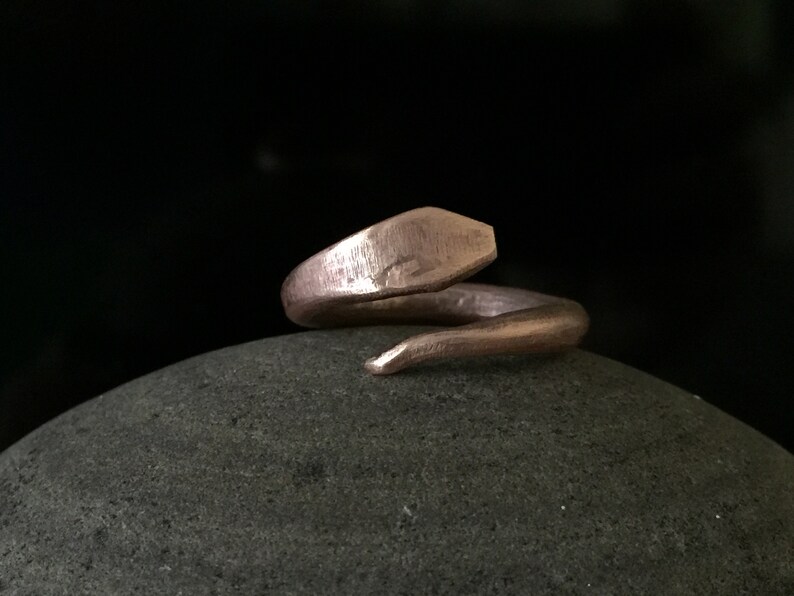 Puede incluir: Un anillo de serpiente de color cobre con un acabado texturizado. El anillo est&aacute; enrollado y la cola es puntiaguda.