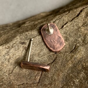 May include: A pair of copper stud earrings with a hammered finish. The earrings are on a wooden surface.