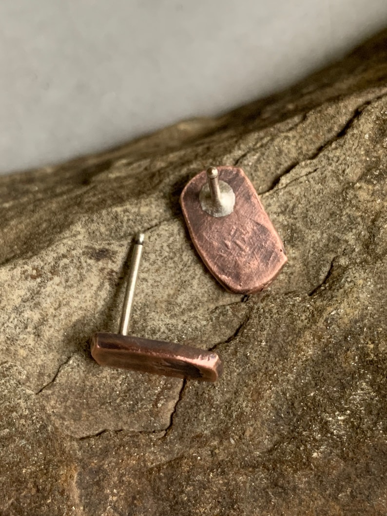 May include: A pair of copper stud earrings with a hammered finish. The earrings are on a wooden surface.