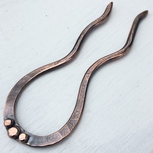 May include: A copper hair clip with a wavy design and three small copper beads at the bottom.