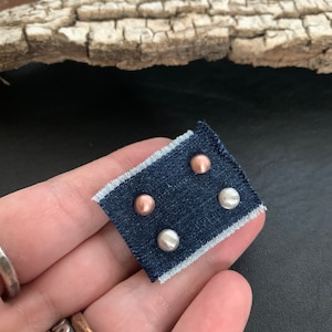May include: Three small round stud earrings on a blue fabric swatch. Two earrings are silver and one is rose gold.