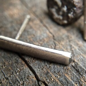 May include: A silver bar earring with a textured surface. The earring is made of metal and has a simple, minimalist design.