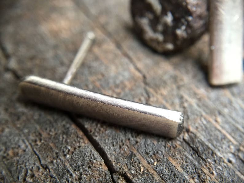 May include: A silver bar earring with a textured surface. The earring is made of metal and has a simple, minimalist design.
