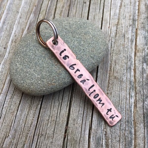 May include: A copper keychain with a silver ring and the text "is breá liom tú" engraved on it.