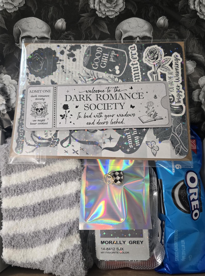 May include: A gift set featuring a variety of items. Includes a sticker sheet with gothic-themed designs, a pair of gray and white striped socks, a small iridescent package with a checkered charm, and a package of Oreo cookies.