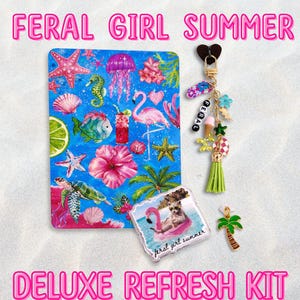 Peut inclure: Un kit Feral Girl Summer Deluxe Refresh comprenant un carnet bleu rectangulaire avec des illustrations tropicales, un porte-clés doré avec des breloques colorées dont un pompon et le mot Feral, et une broche carrée montrant un raton laveur sur une bouée flamant rose.