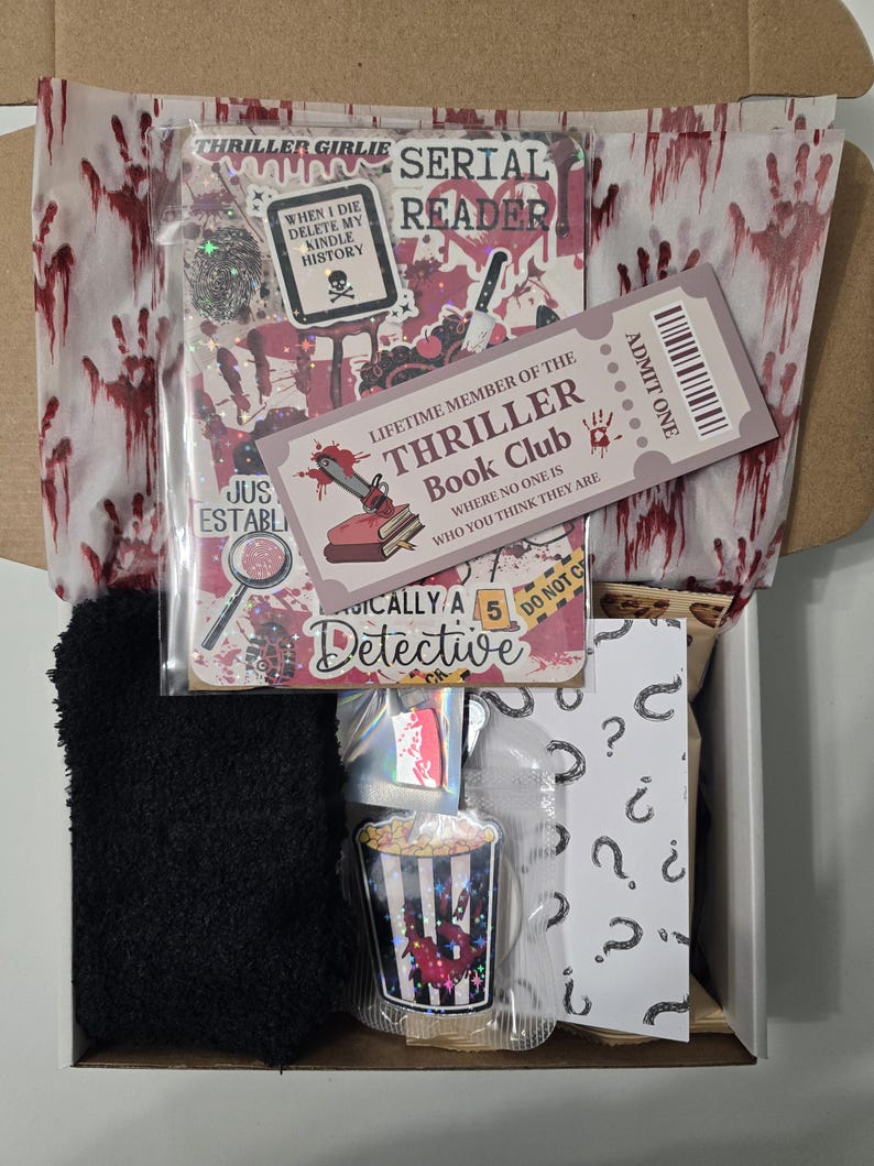 May include: A gift box filled with thriller-themed items. Includes a black fuzzy sock, stickers, a ticket, and a popcorn-themed item. The box is lined with paper featuring bloody handprints and text that reads "Thriller Girlie" and "Serial Reader."