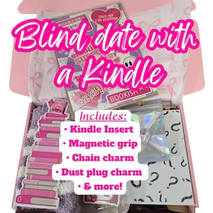May include: A pink box labeled "Blind date with a Kindle" contains a Kindle insert, magnetic grip, chain charm, dust plug charm, and more. The box includes stickers and a stack of pink book-shaped items. The text "GOOD GIRLS READ SMUT" is visible.