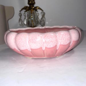 Pode incluir: Uma taça de cerâmica redonda com borda recortada e esmalte de dois tons. A parte inferior da taça é de um rosa sólido, enquanto a borda superior apresenta um esmalte branco salpicado e texturizado que escorre sobre a base rosa em vertical.