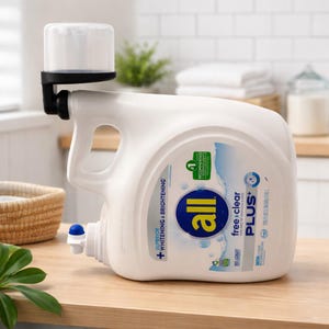 Puede incluir: Una botella grande de detergente blanco con un dispensador negro adjunto en la parte superior. La botella tiene una etiqueta azul y blanca con la marca "all" y las palabras "free clear PLUS+". La botella está sobre una superficie de madera.