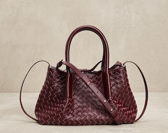 Bolso de mano de piel trenzada color burdeos con asas superiores y correa para llevarlo cruzado.