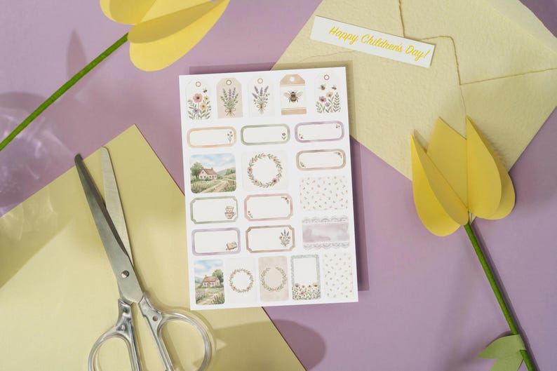 May include: A sheet of decorative stickers with floral and landscape designs, including tags and labels. A pair of scissors and a paper tulip are on a purple surface. A yellow envelope and a card that says "Happy Children's Day!" are also present.