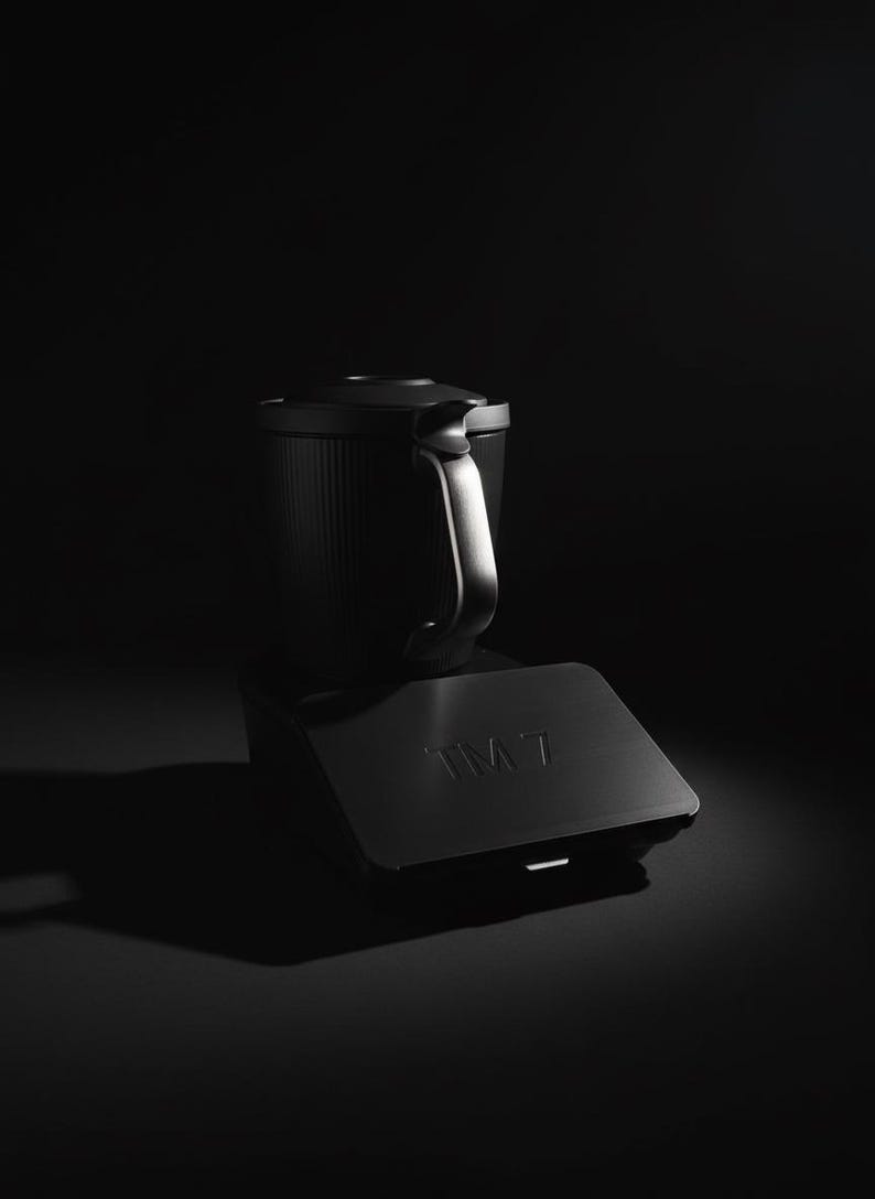 Pode incluir: Uma cafeteira preta com uma al&ccedil;a e uma base. A cafeteira tem um corpo cil&iacute;ndrico com ranhuras verticais. A base tem as letras "IM7" gravadas.
