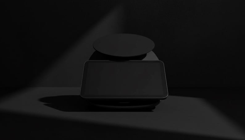 Pode incluir: Uma balan&ccedil;a de cozinha digital preta com uma base retangular e um topo redondo. A balan&ccedil;a est&aacute; sobre um fundo escuro com um efeito de holofote, destacando seu design elegante. &Eacute; usada para medir ingredientes.