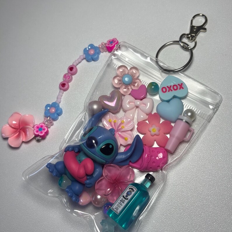 May include: A clear plastic bag filled with various charms, including a blue Stitch figure, pink flowers, hearts, bows, and a miniature bottle. A beaded charm with pink and blue flowers and a silver keychain are also included.