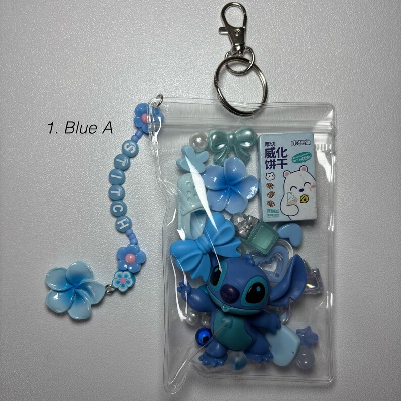 May include: A blue Stitch-themed keychain with a clear plastic pouch containing a Stitch figurine, blue bows, flowers, and a small box with text. The keychain includes a beaded charm spelling "Stitch".