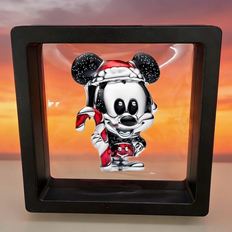May include: A silver Mickey Mouse figurine in a black display case. Mickey is wearing a Santa hat and holding a red and white candy cane. The background is a gradient of orange and yellow.