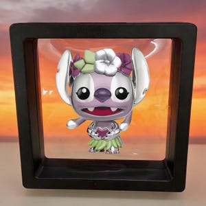 May include: A metallic purple character figurine with large ears, wearing a floral crown of white, green, and purple flowers and a green skirt, holding a small purple heart. The figure is suspended inside a square black floating display frame.