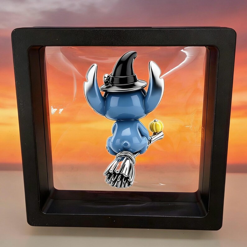 Puede incluir: Una figura de personaje azul con un sombrero de bruja negro, montada en una escoba plateada con una peque&ntilde;a calabaza amarilla, suspendida dentro de un marco de exhibici&oacute;n flotante negro cuadrado sobre un fondo de colores de atardecer.