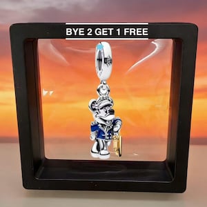 Puede incluir: Un charm de plata con un rat&oacute;n de dibujos animados con uniforme azul y plateado, sosteniendo un objeto dorado. El charm est&aacute; suspendido de una cuenta blanca y plateada. El texto "BYE 2 GET 1 FREE" se muestra encima del charm.