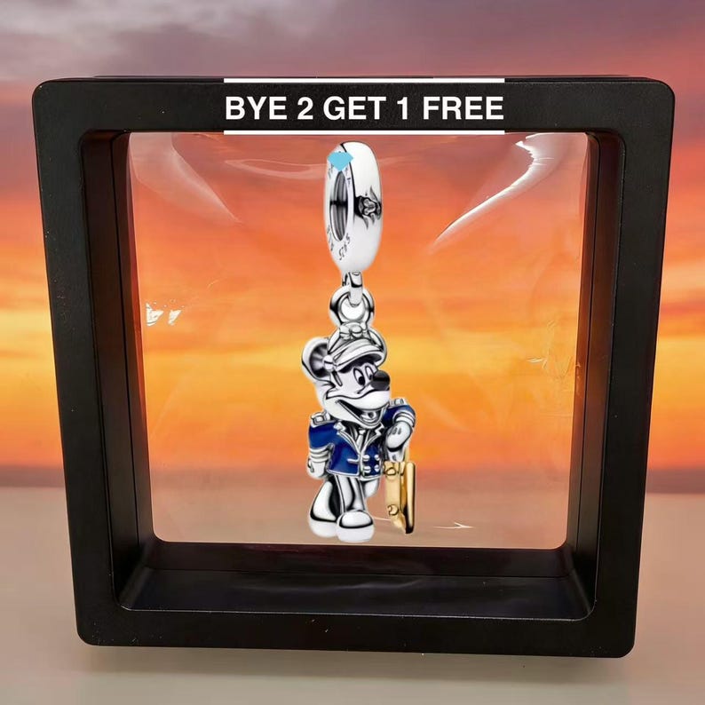 Puede incluir: Un charm de plata con un rat&oacute;n de dibujos animados con uniforme azul y plateado, sosteniendo un objeto dorado. El charm est&aacute; suspendido de una cuenta blanca y plateada. El texto "BYE 2 GET 1 FREE" se muestra encima del charm.