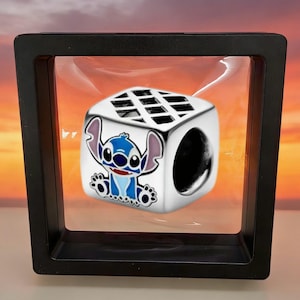May include: A silver-toned cube-shaped bead featuring a colorful enamel graphic of the character Stitch on the front face. The bead has a grid pattern on the top surface and a circular hole through the center for threading onto a bracelet or chain.