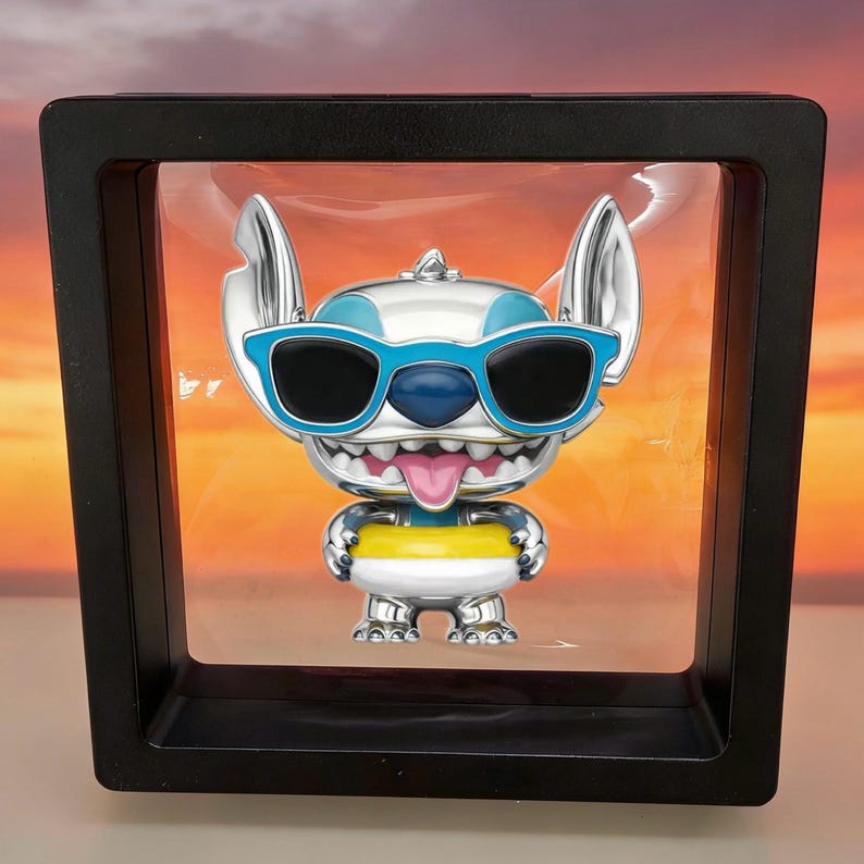 K&ouml;nnte beinhalten: Eine silberfarbene Sammlerfigur der Figur Stitch mit gro&szlig;en Ohren, blauer Sonnenbrille und herausgestreckter rosa Zunge, die in einem quadratischen schwarzen Schwebekader pr&auml;sentiert wird. Die Figur tr&auml;gt einen gelb-wei&szlig;en Schwimmring um die Taille.