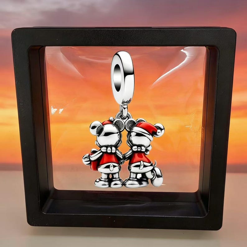 Pode incluir: Um pingente de prata com duas figuras de rato de desenho animado usando gorros de Papai Noel vermelhos e roupas vermelhas, em p&eacute; lado a lado. As figuras s&atilde;o feitas de prata polida com detalhes em esmalte vermelho e presas a uma argola.