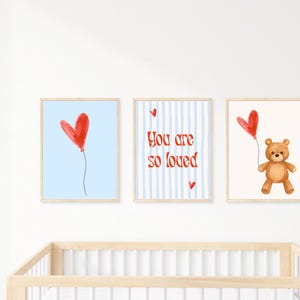Könnte beinhalten: Drei gerahmte Kunstdrucke mit einem Kinderzimmer-Thema. Einer zeigt einen roten Herzballon auf hellblauem Hintergrund. Ein anderer sagt "You are so loved" mit gestreiftem Hintergrund. Der dritte zeigt einen Teddybären, der einen roten Herzballon hält.