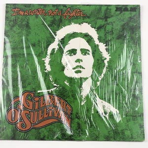 May include: A vintage vinyl record album cover featuring a green background with a white portrait of a person. The album title "Gilbert Sullivan" is in orange and brown lettering. The text "I'm a writer, not a fighter" is at the top.