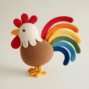 May include: A handcrafted crochet rooster in a whimsical design. The rooster features a brown body, white head, red comb and wattle, yellow beak and feet, and a rainbow tail. This decorative item is perfect for a nursery or as a unique home accent.