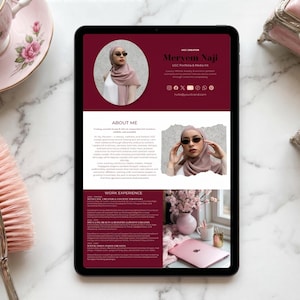 Può includere: Un tablet digitale che mostra un curriculum vitae con il nome Mervem Naji. Il tablet è su una superficie di marmo, accanto a una tazza e un piattino rosa, un pennello per il trucco rosa e un piccolo portagioie. Il curriculum ha uno sfondo bordeaux.