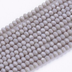 May include: A strand of light gray faceted glass beads. The beads are round and have a smooth, polished finish.