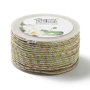 May include: Spool of multi-colored jewelry cord. The cord is a mix of yellow, green, and pink threads, tightly wound. The clear plastic container has a white label with Chinese characters and the words "Jewellery cord".