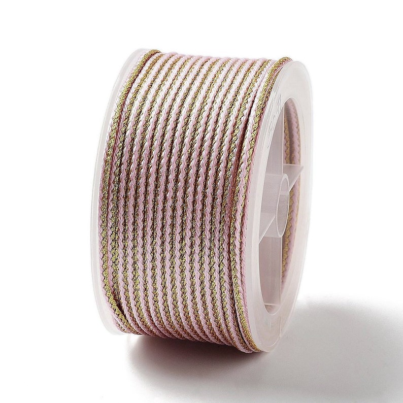 Puede incluir: Carrete de cord&oacute;n trenzado rosa y dorado. El cord&oacute;n est&aacute; enrollado firmemente en un carrete de pl&aacute;stico transparente. El cord&oacute;n tiene un centro rosa con bordes dorados, creando un patr&oacute;n de rayas. Ideal para la fabricaci&oacute;n de joyas y manualidades.