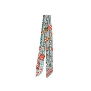 May include: A narrow, decorative scarf with a repeating pattern of keys, hearts, and other ornate designs in red, orange, and green on a light gray background. The scarf is tied in a knot, showcasing its intricate details and color palette.