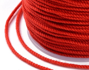 Puede incluir: Una bobina de cordón rojo brillante, enrollada apretadamente, con algunos hilos de cordón sueltos delante de la bobina.