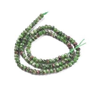 May include: A strand of green and pink gemstone beads. The beads are faceted and have a speckled appearance. The beads are strung on a green thread.