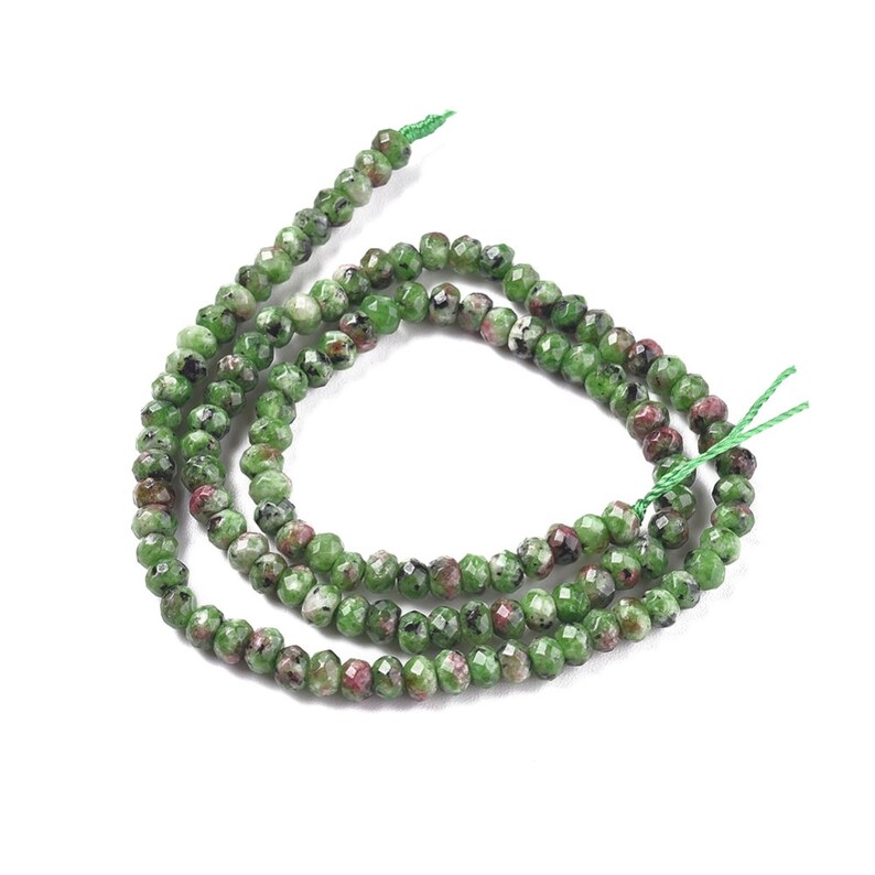 May include: A strand of green and pink gemstone beads. The beads are faceted and have a speckled appearance. The beads are strung on a green thread.