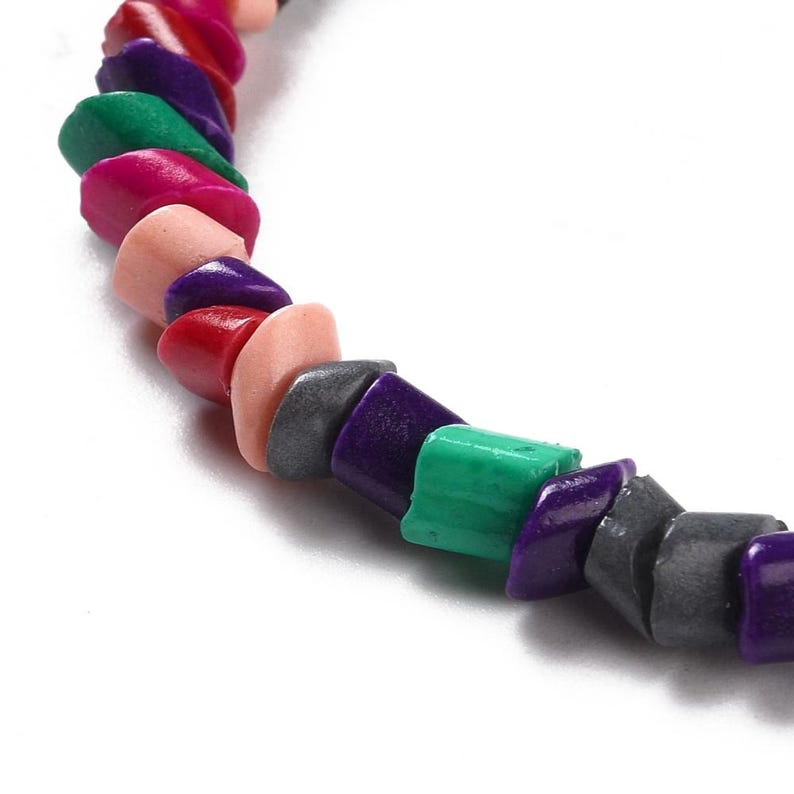 May include: A colorful beaded necklace with a mix of pink, red, purple, green, and gray beads. The beads are all different shapes and sizes, and they are strung together in a random pattern.