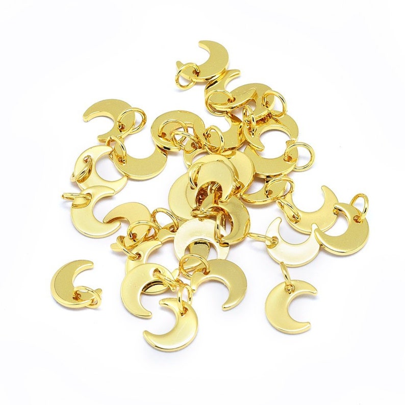 May include: A group of gold-colored crescent moon charms with jump rings. The charms are scattered on a white surface.