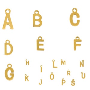 Może przedstawiać: Złote metalowe zawieszki w kształcie liter alfabetu. Pokazane są litery od A do T, z wyjątkiem litery Q.