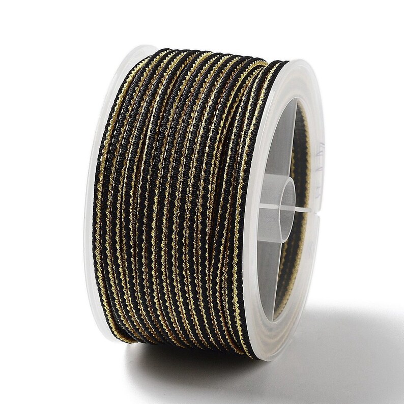 May include: A spool of black and gold cord with a white plastic bobbin. The cord is wound tightly around the bobbin.
