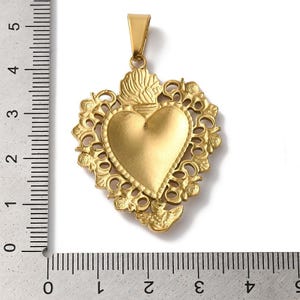 K&ouml;nnte beinhalten: Goldfarbener Anh&auml;nger mit herzf&ouml;rmigem Mittelteil, umgeben von einem verzierten Rand im Filigranstil. Der Anh&auml;nger hat eine &Ouml;se zum Anbringen an einer Kette. Der Anh&auml;nger ist etwa 5 cm lang.